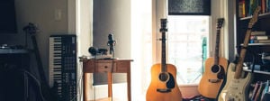 Musikkrom med oppsett av forskjellige instrumenter som gitar og keyboard, samt også headet og mikrofon på et bord. På høgre side er det en bokhylle med bøker